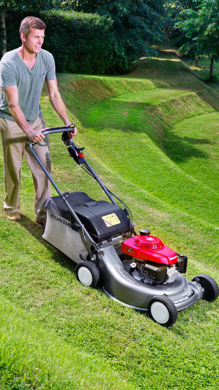Grasmaaier, driekwart vooraanzicht, zicht op rechterkant, in gebruik door model, tuinlocatie.