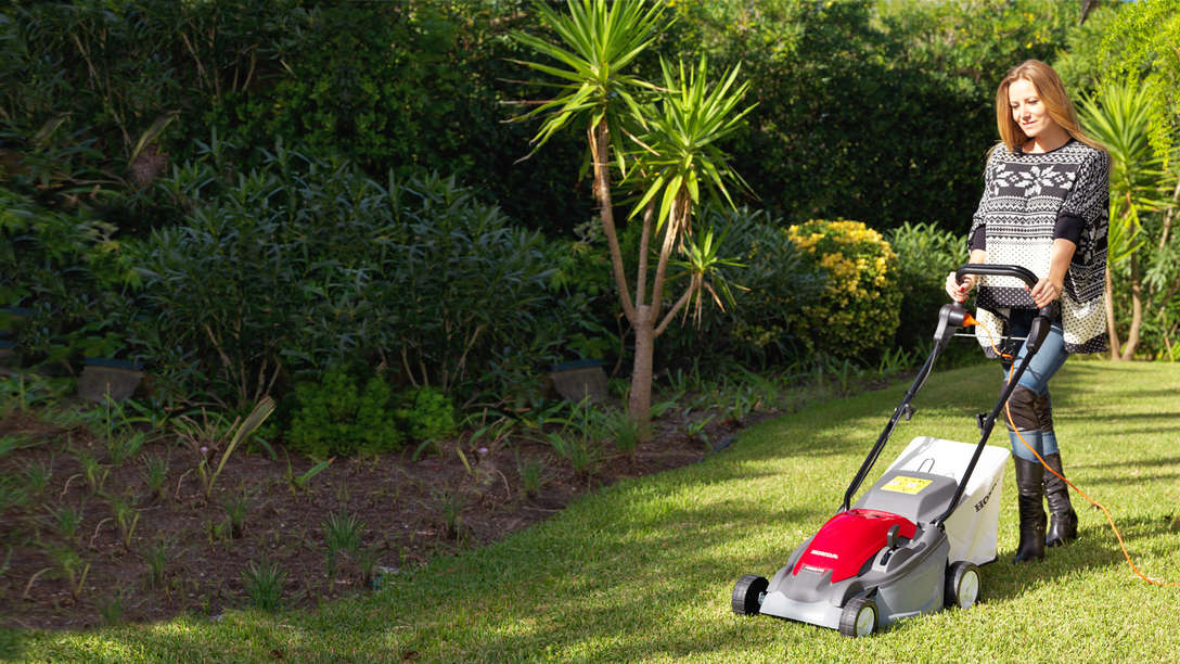Honda HRE-grasmaaier, driekwart vooraanzicht, zicht op linkerkant, in gebruik door model, tuinlocatie.