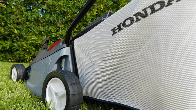 Honda HRE-grasmaaiers, driekwart achteraanzicht, close-up van grasvangzak, tuinlocatie.