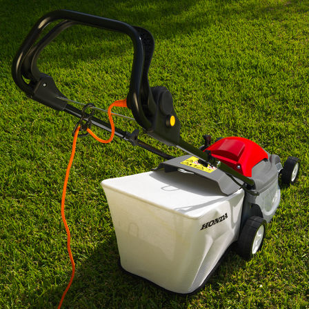 Honda HRE-grasmaaiers, driekwart achteraanzicht, gericht op snoer, tuinlocatie.