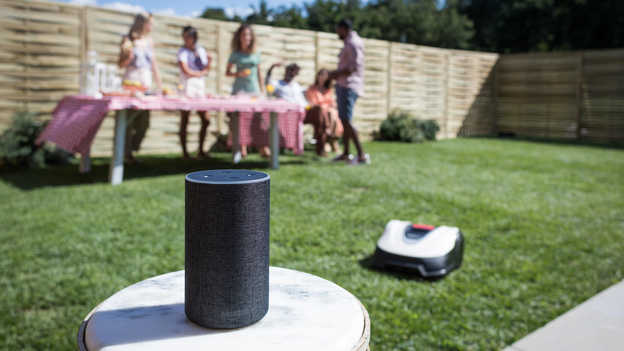 Close up van Amazon Alexa met Miimo en tuinfeest op de achtergrond op het gazon.