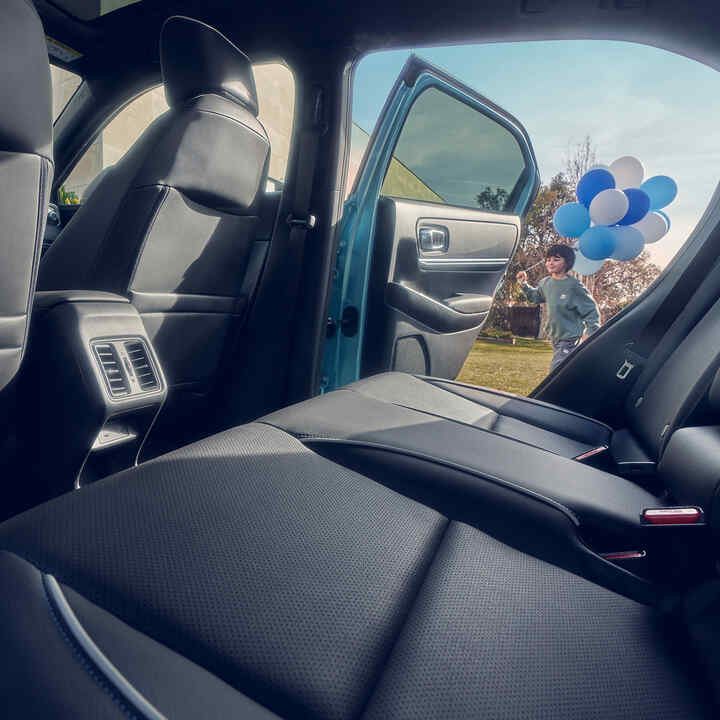 Close-up van de achterzetel in de Honda e:Ny1 met een kind met ballonnen dat langs de openstaande deur loopt.