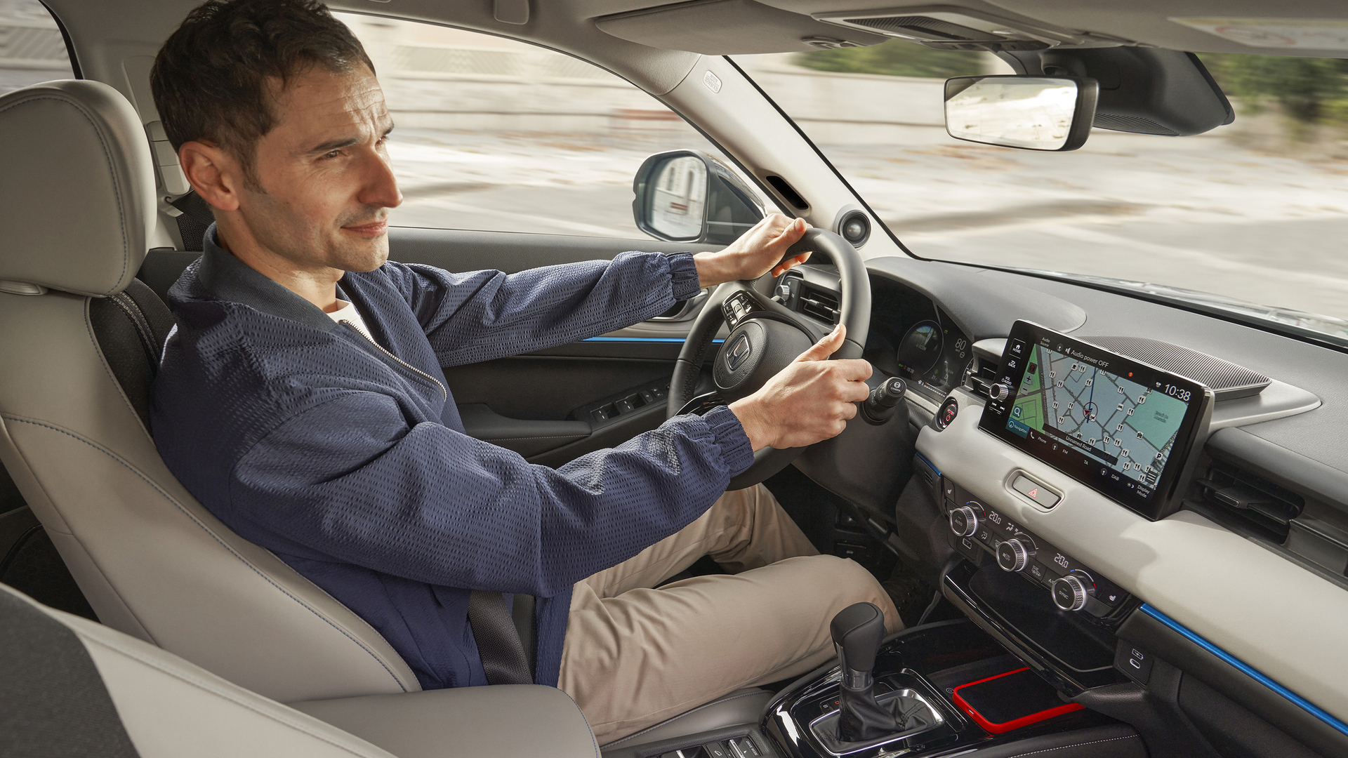 A driver sits behind the wheel of a Honda HR-V, viewed from the front passenger side, with the interior dashboard and a navigation map displayed on the center screen.