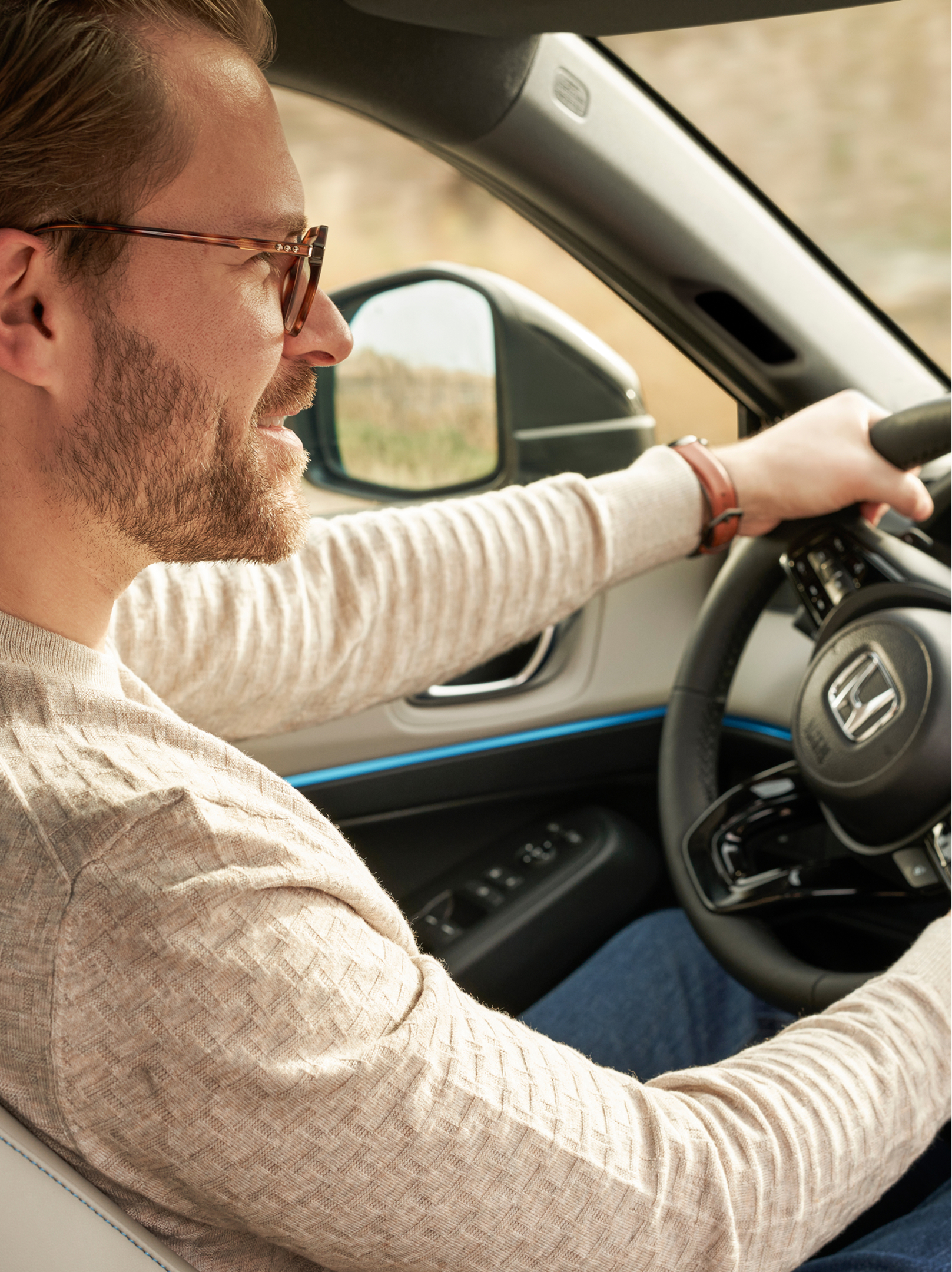 A man wearing glasses drives a Honda HR-V, shown from the front passenger seat, with both hands on the steering wheel and the dashboard visible.