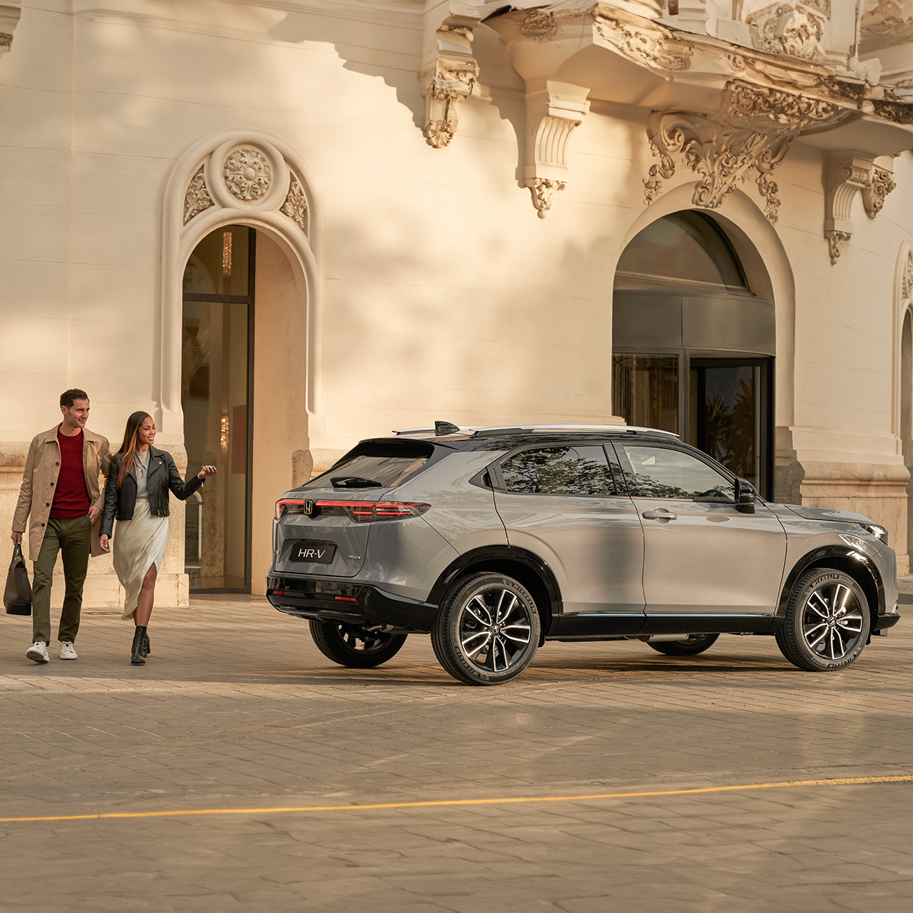 Zijaanzicht van de Honda HR-V buiten een hotellocatie, met een koppel dat langsloopt.