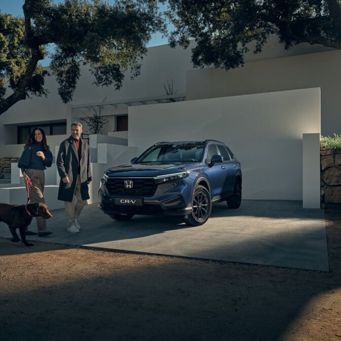 Couple walking a dog next to a parked Honda CR-V.