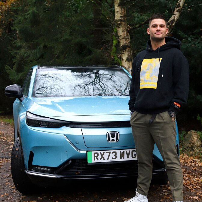 Influencer standing in front of Honda e:Ny1 in forest location.