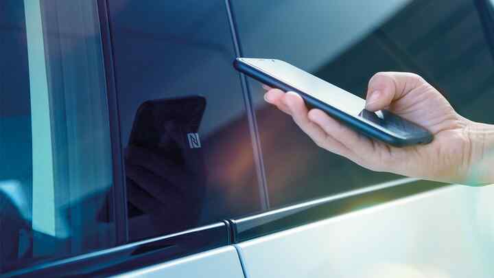 Close-up van My Honda+ app op smartphone van persoon naast auto