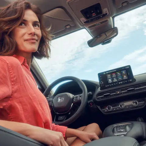 Vrouw zit op de bestuurderszetel en gebruikt het infotainmentscherm van de Honda ZR-V hybride.