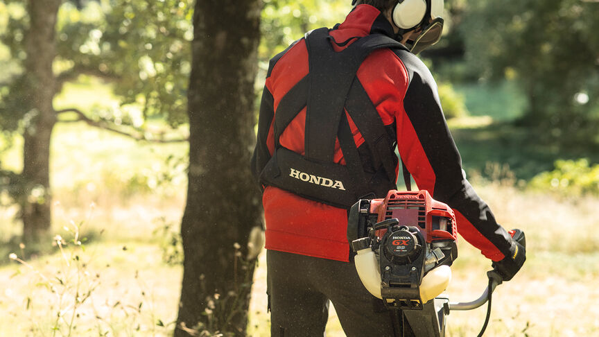 Model met ruggedragen bosmaaier op boslocatie.