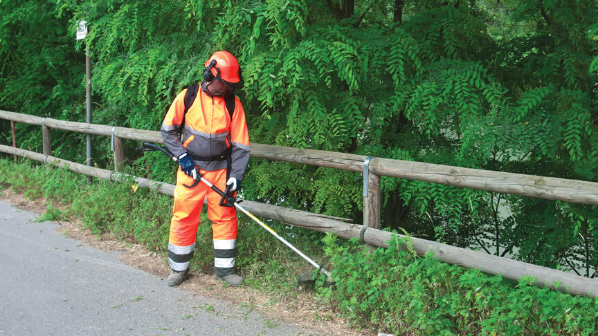 Model met ruggedragen bosmaaier op boslocatie.