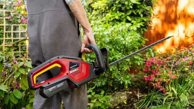 Model met draadloze Honda-heggenschaar in een tuin.