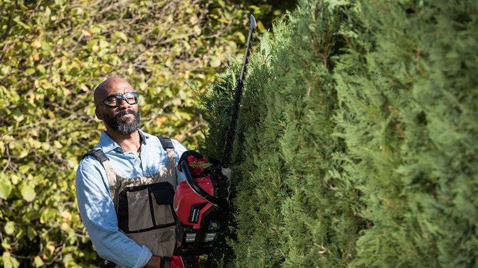 Front view of a model with Honda cordless hedge trimmer in a garden.