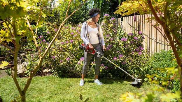 Vrouw in tuinomgeving gebruikt Honda accugazontrimmer.