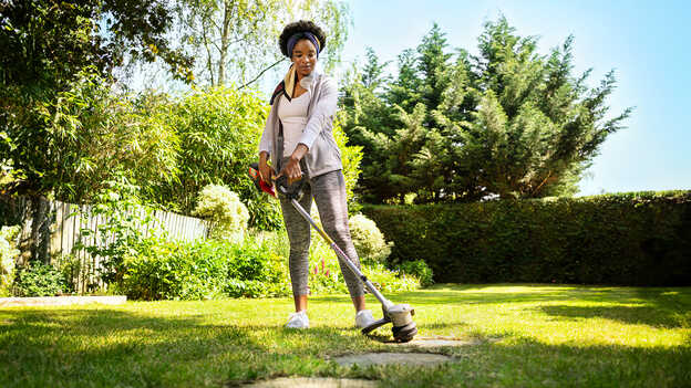 Vrouw gebruikt Honda accugazontrimmer op gras in een tuinomgeving.