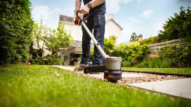 Man gebruikt Honda accugazontrimmer op gras in een tuinomgeving.