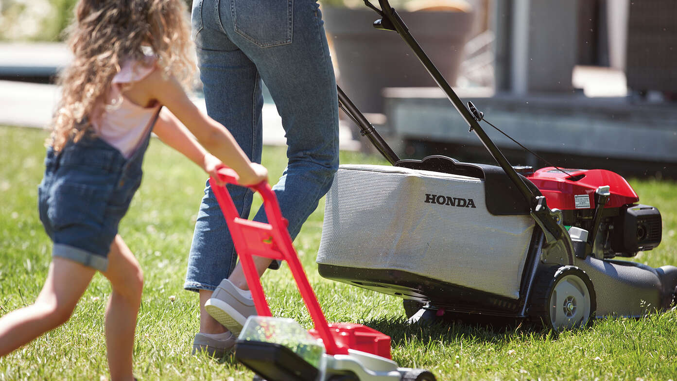 Honda IZY grasmaaier zijaanzicht met vrouw en kind in tuinomgeving