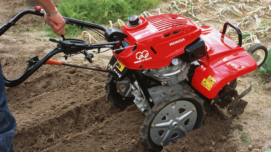 Vooraanzicht roterende tuinfrees aan het werk op het land.