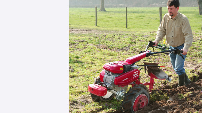 Tweewielige trekker met ploeghulpstuk, in gebruik door model, tuinlocatie.