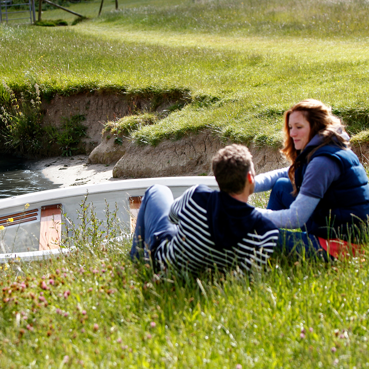 Twee personen zitten aan de oever naast een boot in het water.