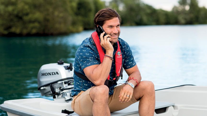 Man op kleine boot die zijn telefoon oplaadt via de buitenboordmotor tijdens het praten