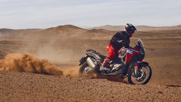 Model rijdend op een CRF1100L Africa Twin motorfiets op een woestijnlocatie.