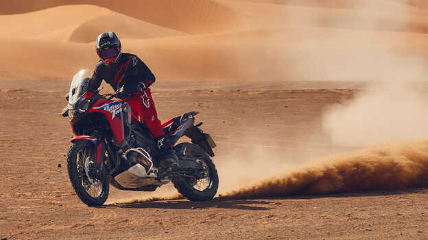 Model rijdend op een CRF1100L Africa Twin motor op een woestijnlocatie.