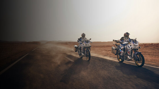 Rijders in driekwart vooraanzicht op Honda CRF1100 Africa Twin Adventure Sports op een weg in woestijnomgeving. 