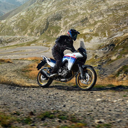 XL750 Transalp op gravelpad met bergen in achtergrond.