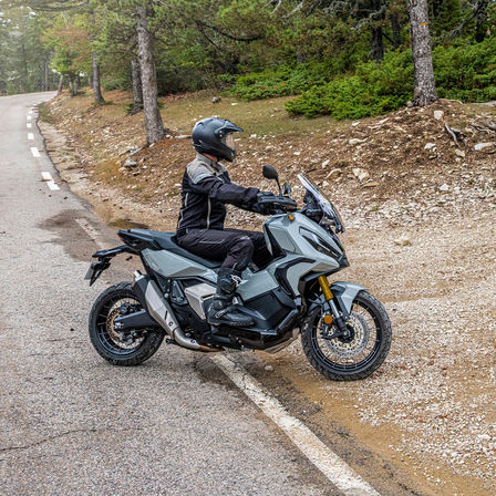 Honda X-ADV, driekwart vooraanzicht, met rijder, grijze motor, bosweg