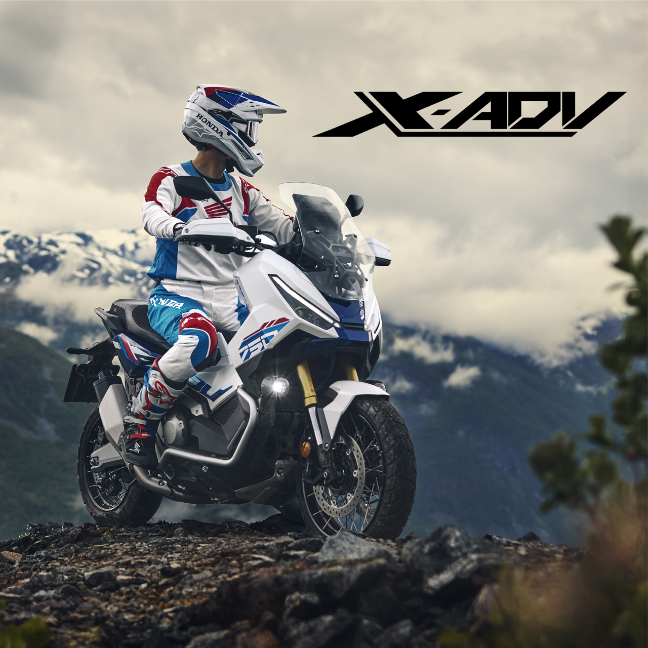 A Honda X-ADV motorcycle on a rocky mountain terrain with snow-capped peaks in the background. The rider is wearing colorful racing gear and a helmet. The X-ADV logo is displayed prominently in the upper right corner of the image.
