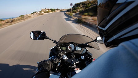 Zicht over de schouder van de motorrijder, van motorfietsinstrumenten, stuur en de weg voor (locatie).