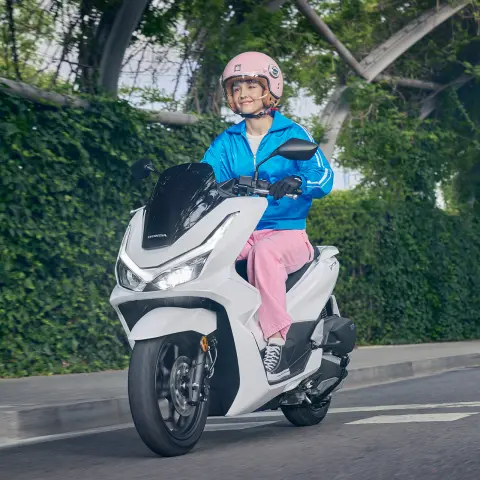 Model rijdend op een PCX125 motorfiets in de stad.