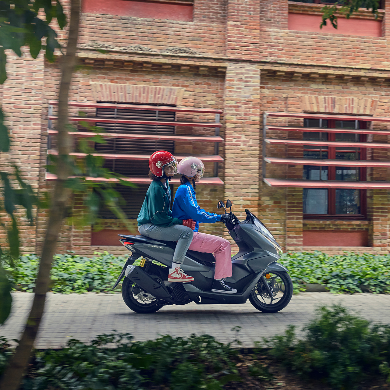 Zijaanzicht van modellen rijdend op de PCX125 in een stadsomgeving.