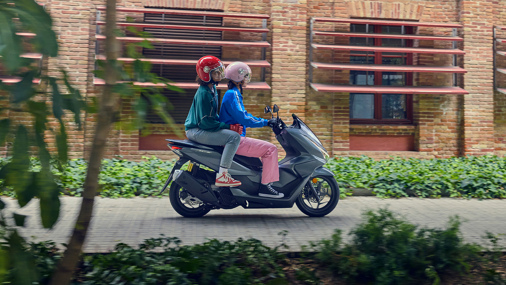 Zijaanzicht van modellen rijdend op de PCX125 in een stadsomgeving.