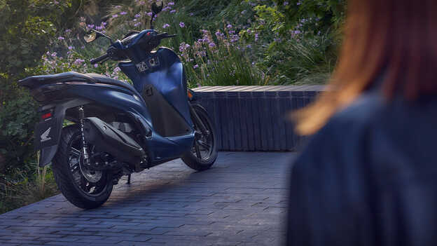 Achteraanzicht van de Honda SH350i in een tuin. 