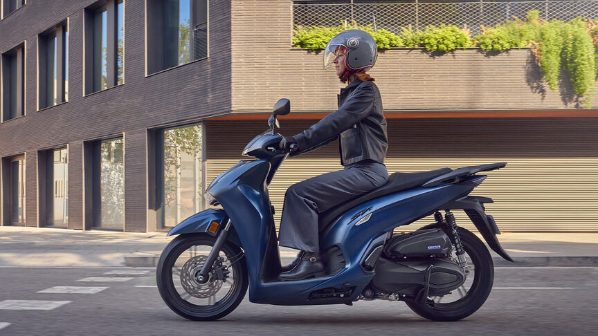 Dame rijdt in de stad op een Honda SH350i in zijdelings aanzicht.