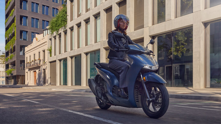 Dame rijdt in de stad op een Honda SH350i in zijdelings aanzicht.