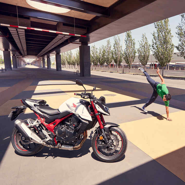 Honda CB750 Hornet onder een brug met een man die breakdancet.
