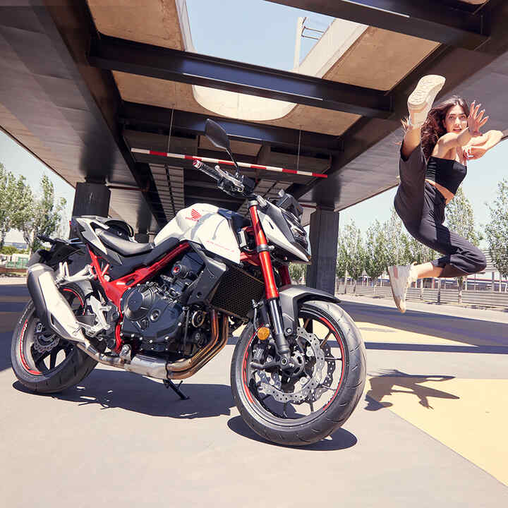 Vrouwelijke danseres springt in de lucht naast een Honda CB750.