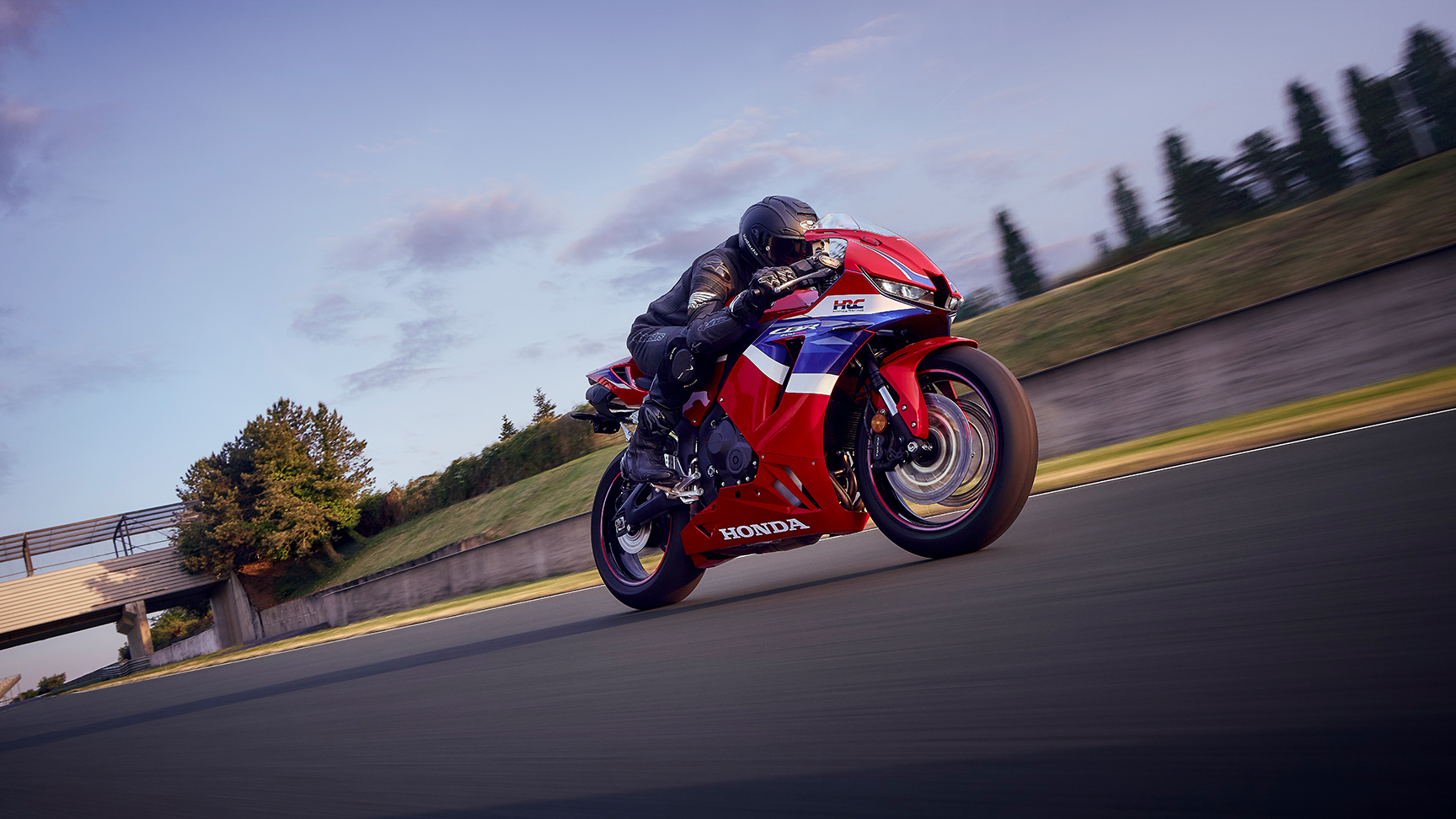CBR600RR met rijder op circuit in de bocht bij zonsondergang.