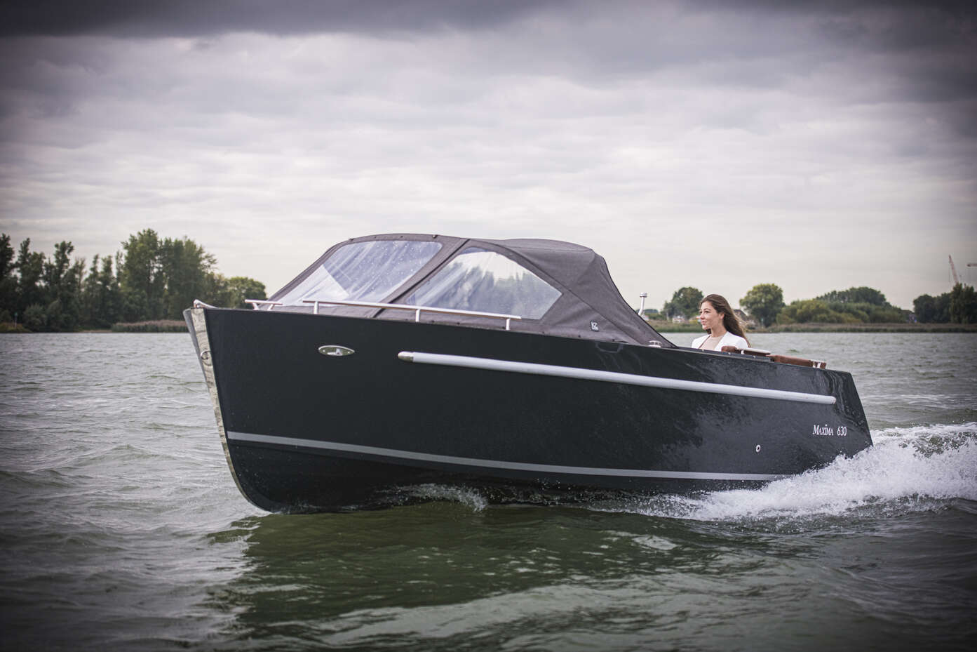 side view of man steering maxima sloop boat on the water