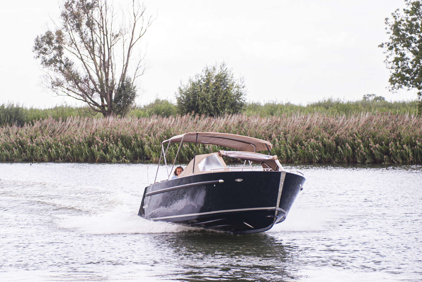 view from behind of man steering maxima sloop boat on the water