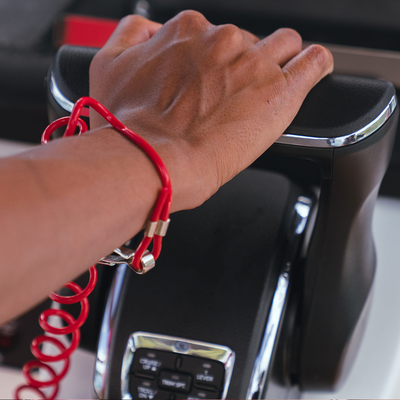A hand wearing a red coiled wristband grips the handlebar of a Honda motorcycle, with part of the instrument panel visible below.